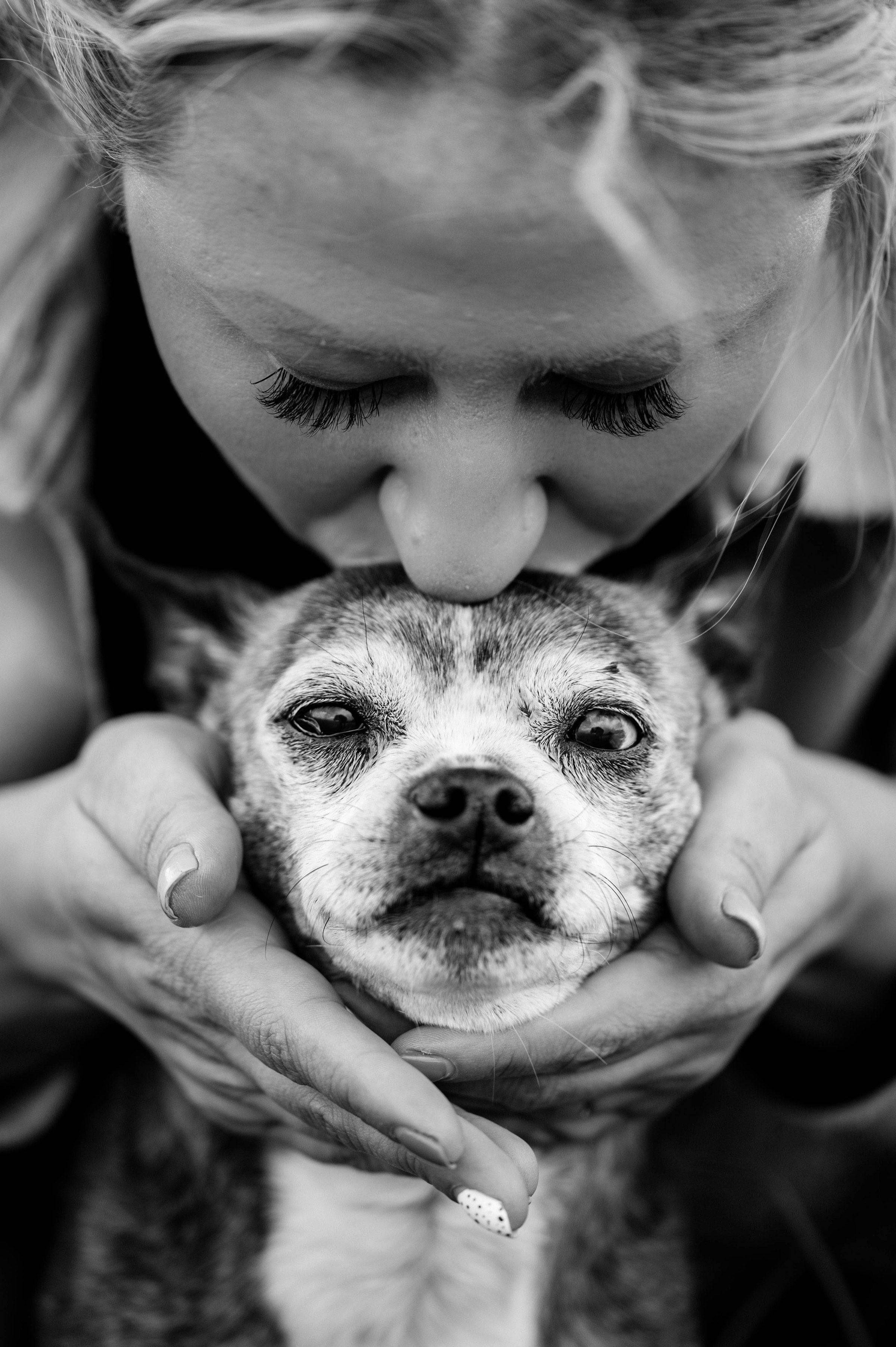 A woman kissing the head of her elderly dog